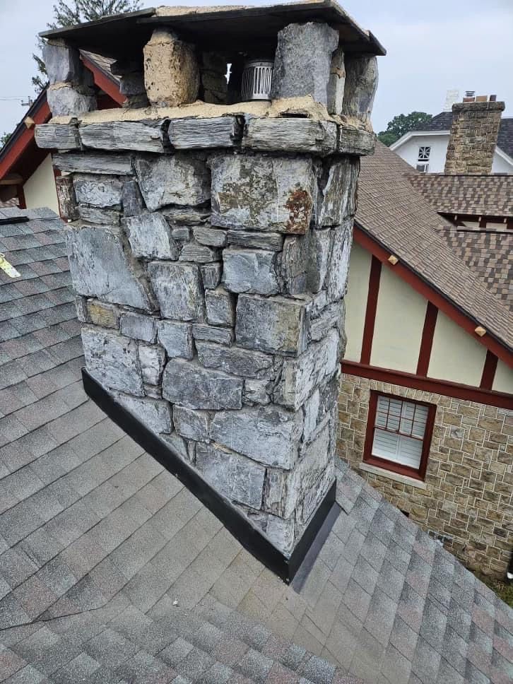 A stone chimney is on the roof of a house.