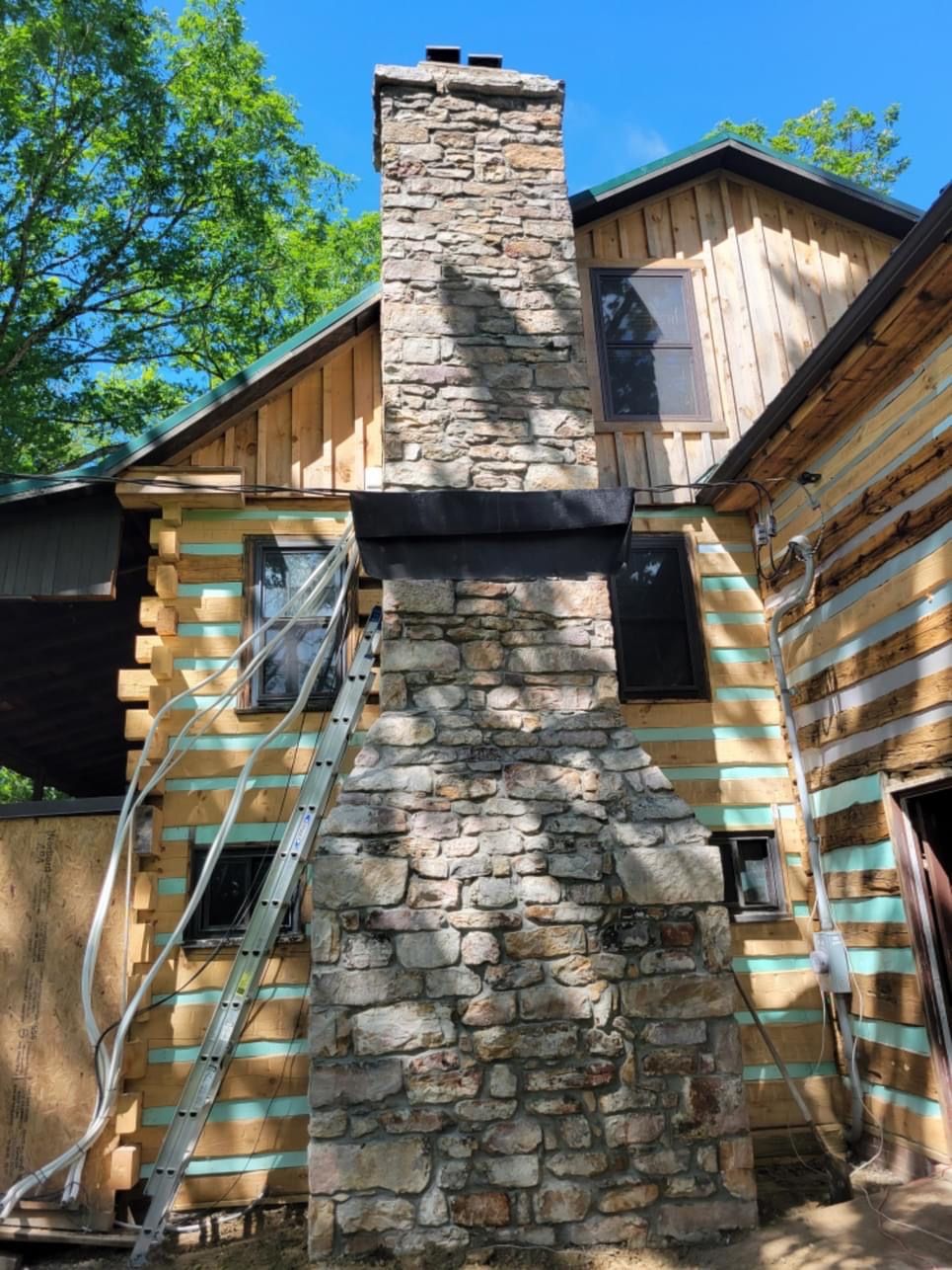 A large stone chimney is on the side of a log cabin.