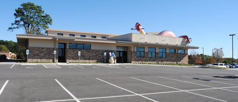Exterior view of a building with a parking lot, under a blue sky. A whimsical roof structure is visible.