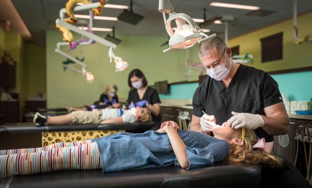 Dentist examining child's teeth. Other children are getting dental work, in a bright, kid-friendly office.