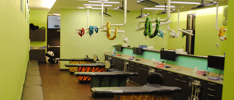 A child's dental office with chairs and tools in a brightly colored room. A panda sits in the back.