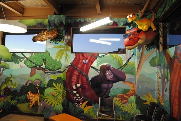 Jungle-themed dental office with painted murals, two TVs, and dinosaur sculptures.