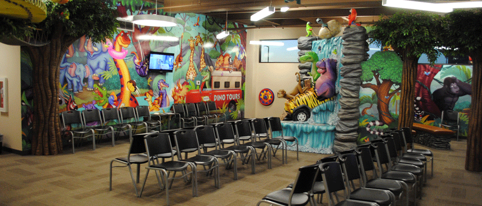 A brightly decorated room with a jungle theme, rows of chairs, and a small TV.