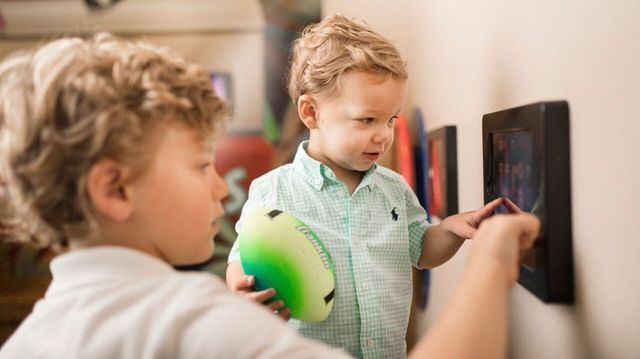 Two young boys interact with a wall display in a museum setting. One touches the screen.