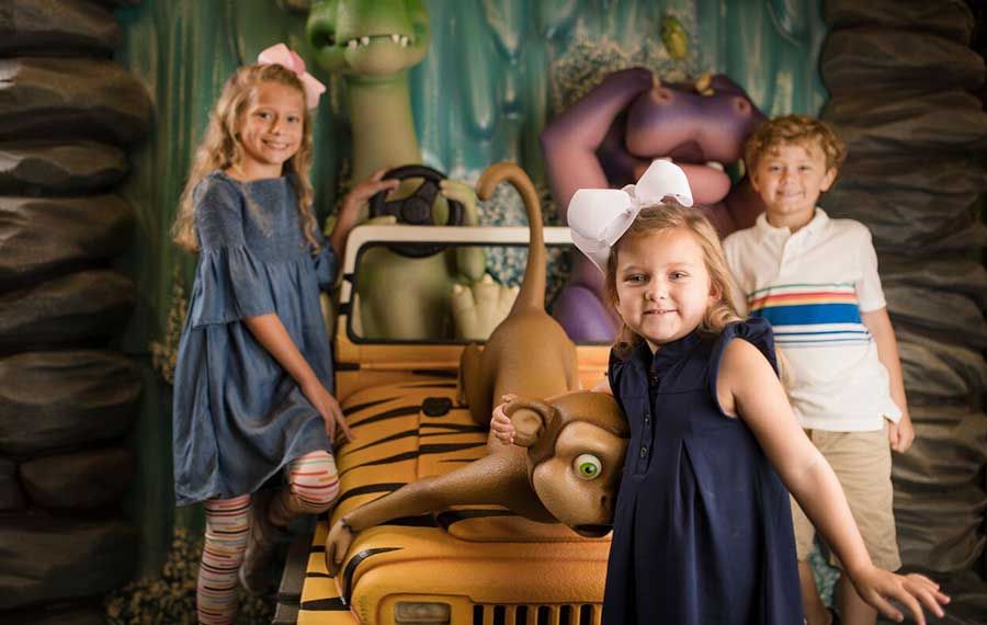 Three children pose with cartoon animal figures and a yellow jeep.