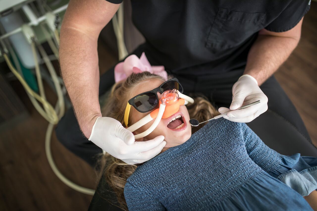 Dentist placing an oxygen mask on a young girl's face. Girl is in a dental chair.