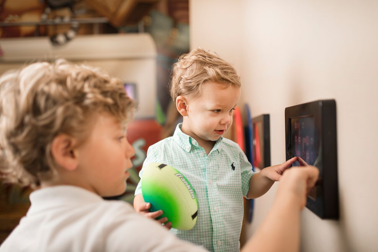 Two young boys looking at an art display on a wall, one holding a green ball.