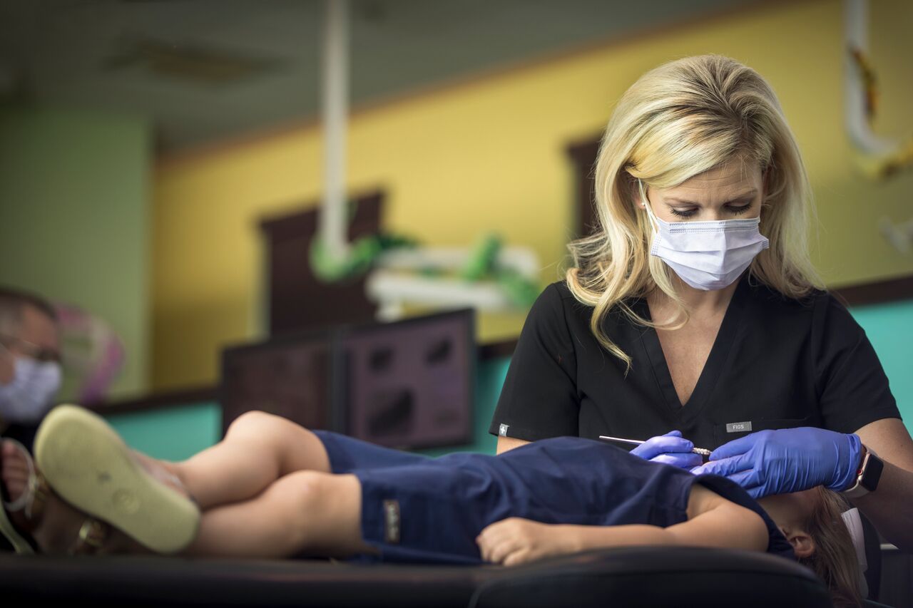 Dentist in mask and gloves examining a child's teeth in a dental office.