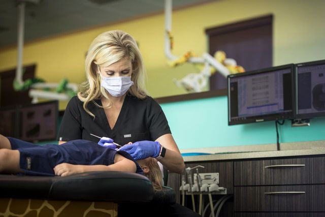 Dentist in mask and gloves examining a child's teeth in a dental office.