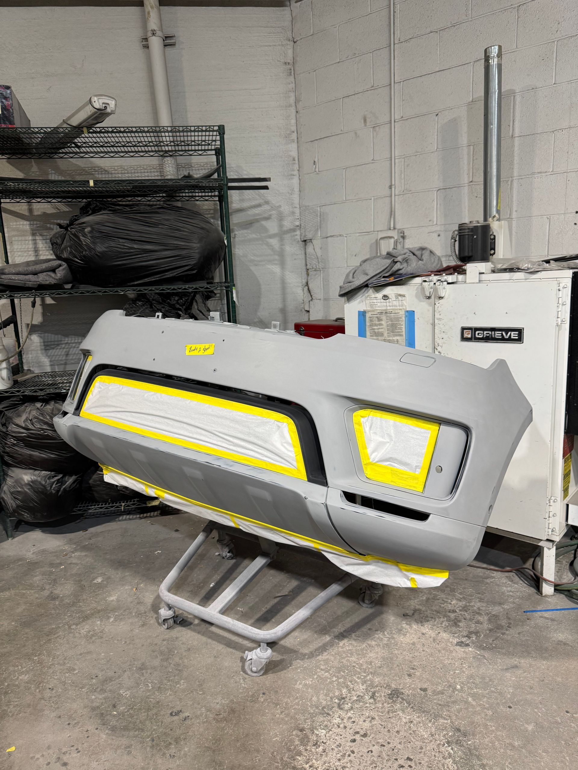 Gray industrial machine with yellow accents on a wheeled stand in a workshop, next to a white cabinet