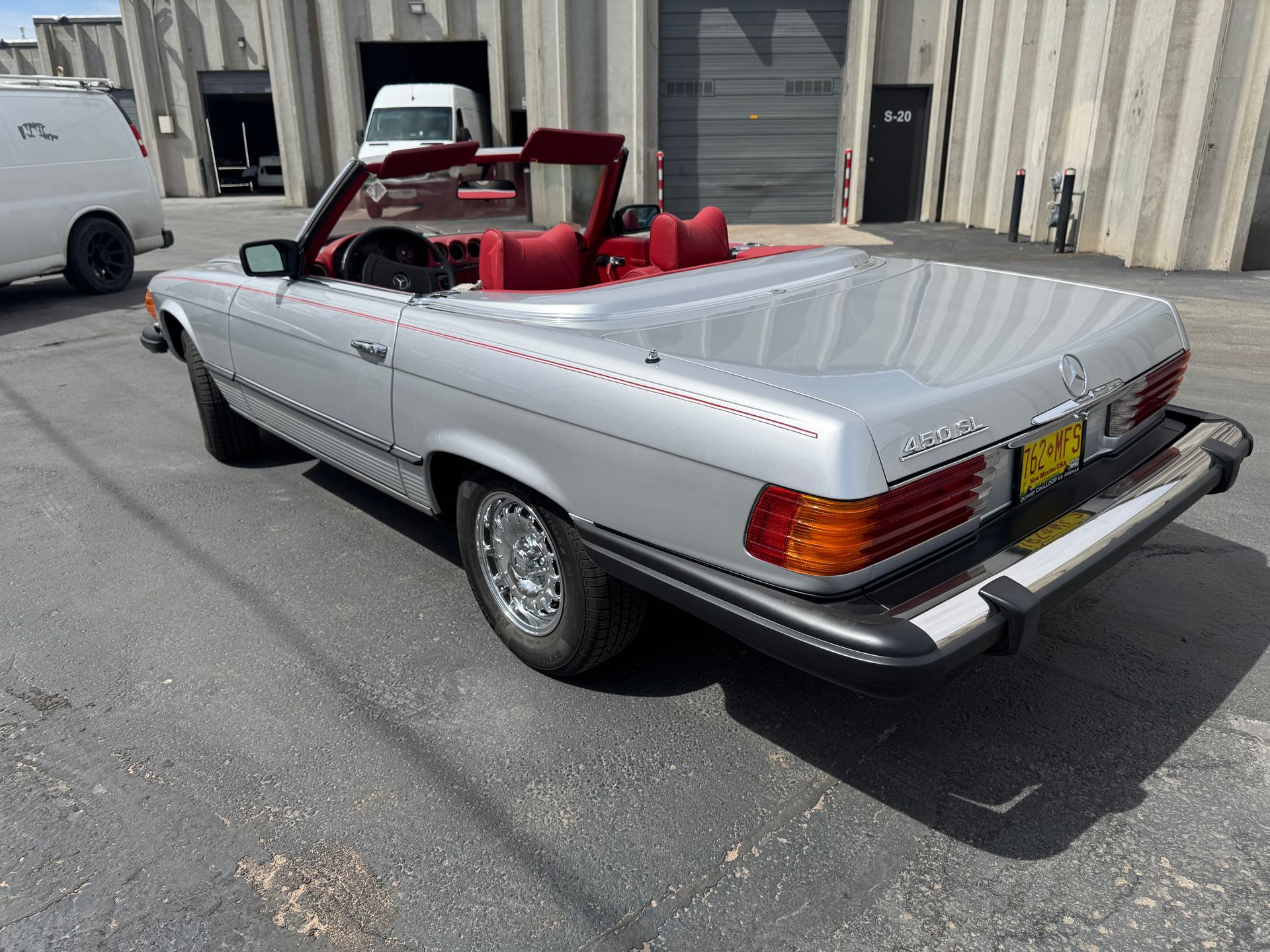 Silver convertible classic car with red interior parked in a lot, rear three-quarter view