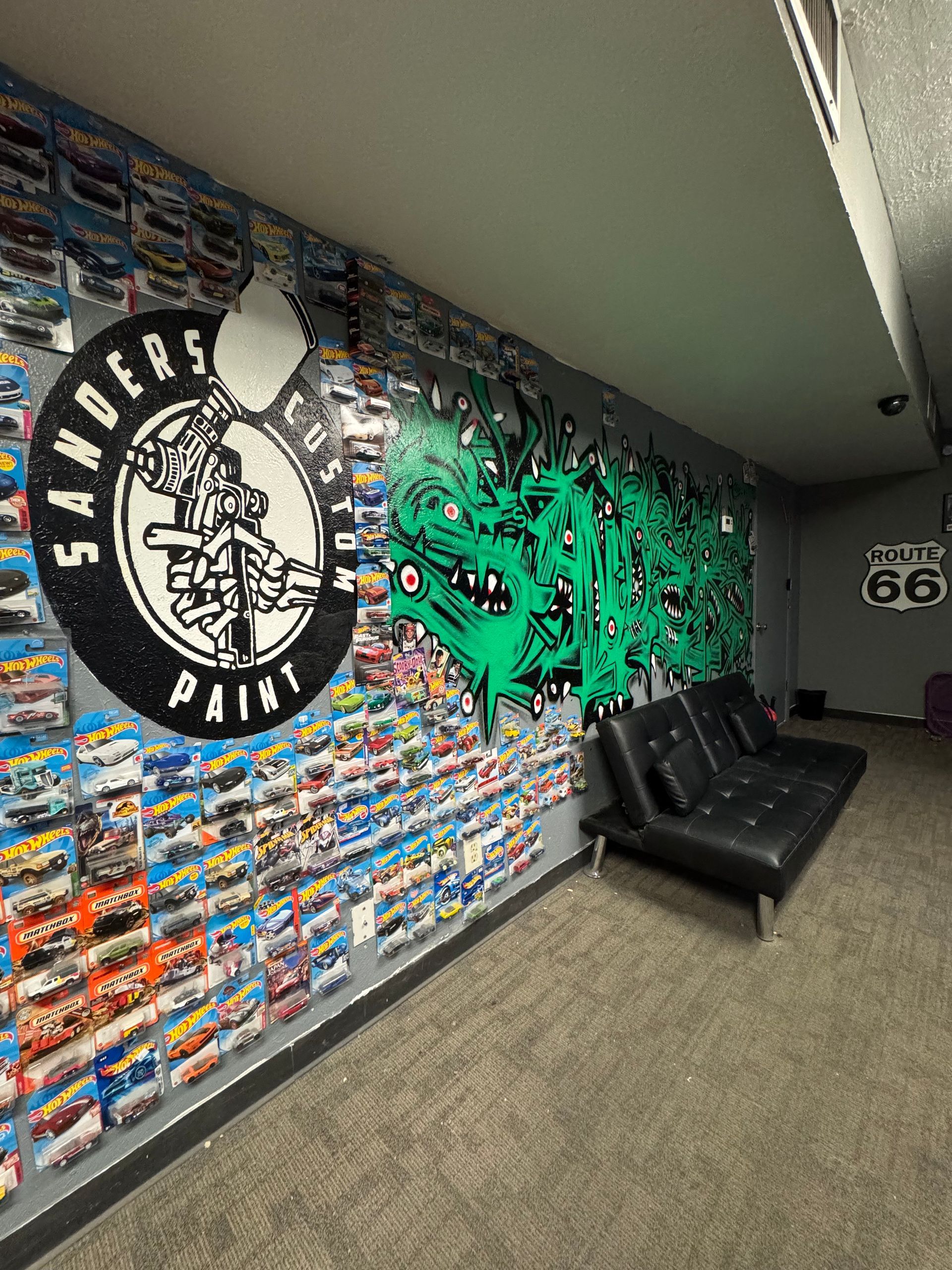 Hallway lounge with graffiti wall art, black couch, and gray carpet under slanted ceiling.