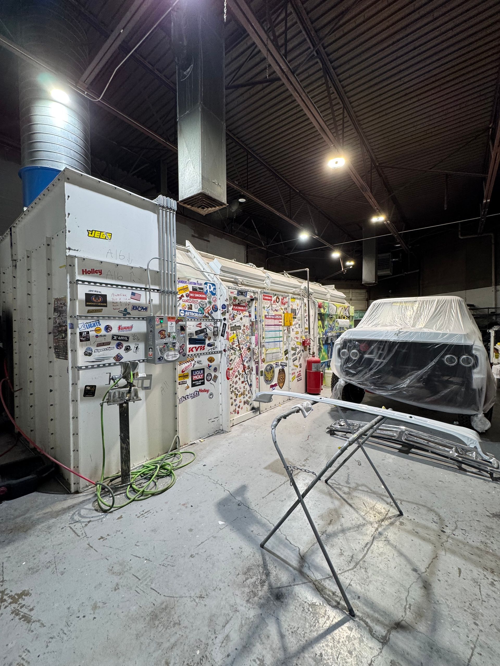 Art studio with paint-splattered walls, hanging lights, and a covered object on a stand in the foreground