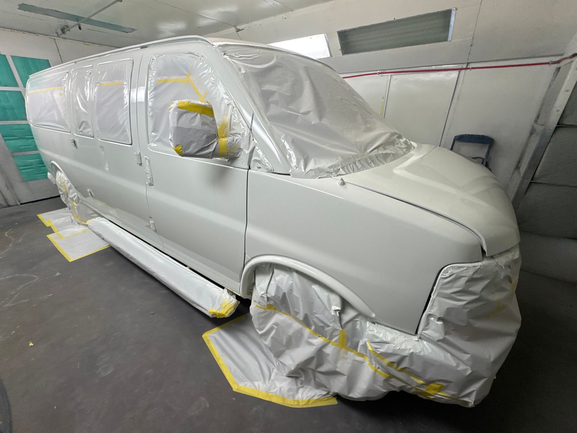 White van masked with protective plastic in a paint booth, awaiting refinishing.