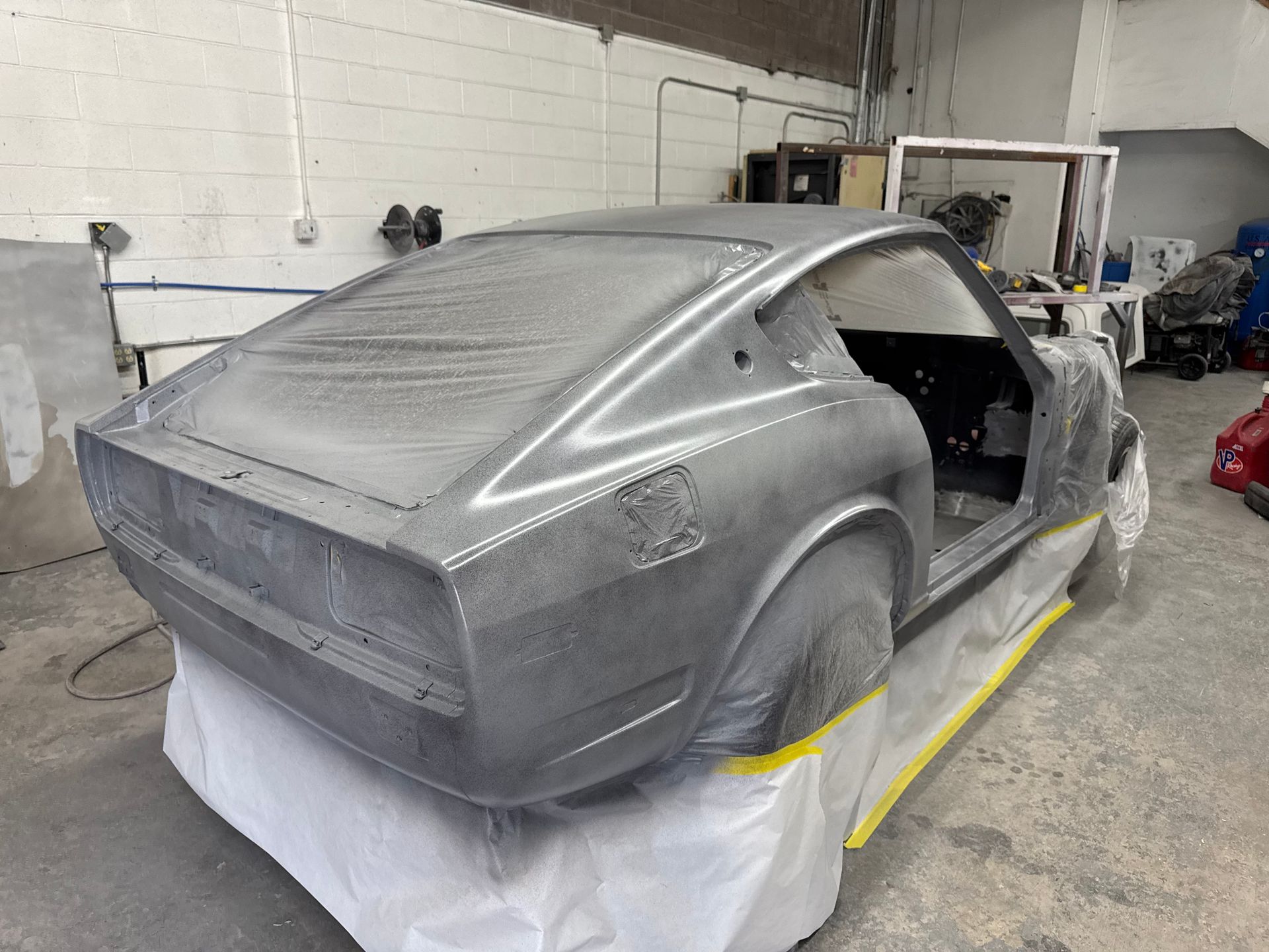 Gray sports car body shell in an auto shop, masked with plastic and tape during paint prep