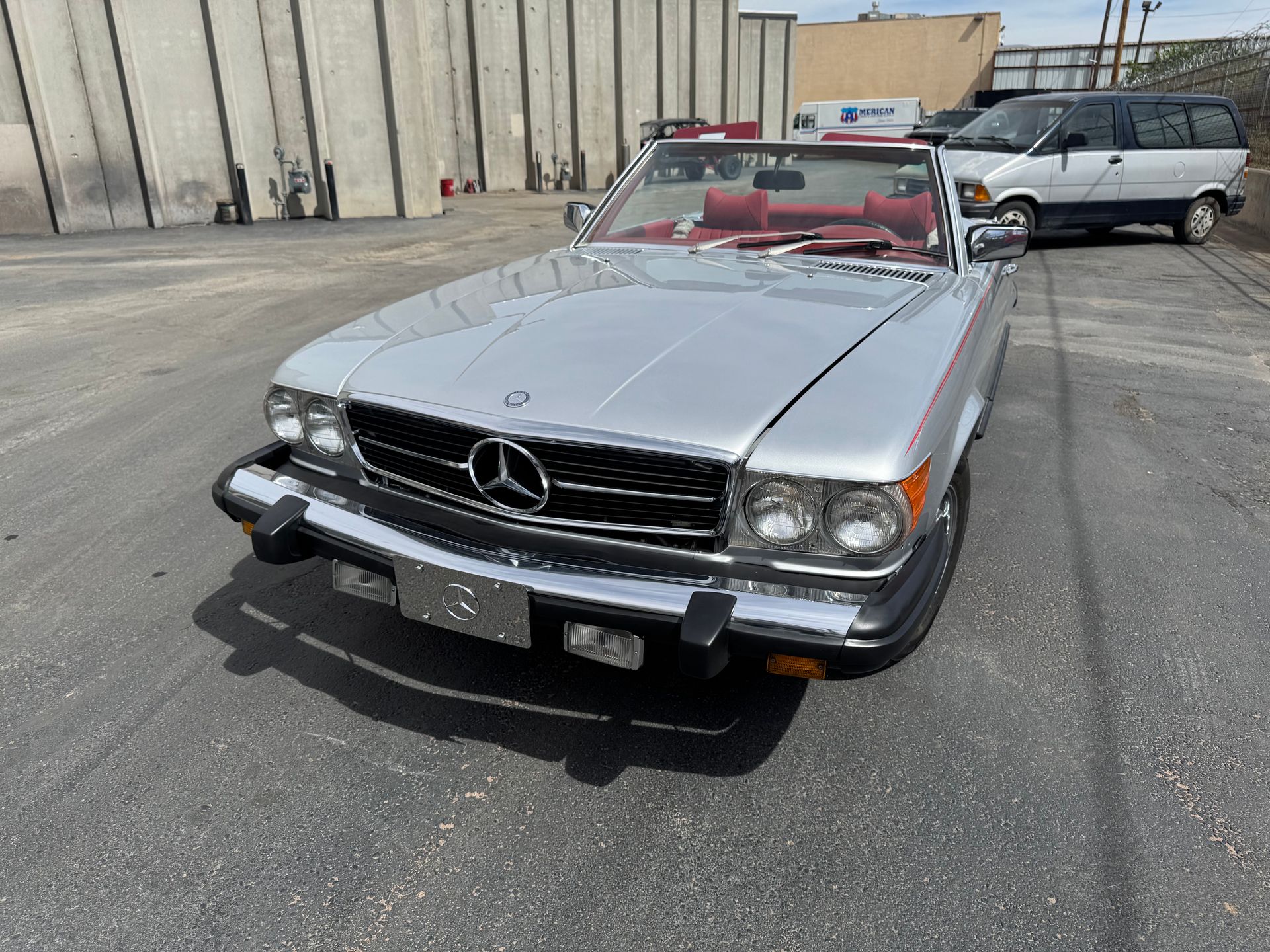 Silver Mercedes convertible parked in an industrial lot, front view with red interior and another car behind it.