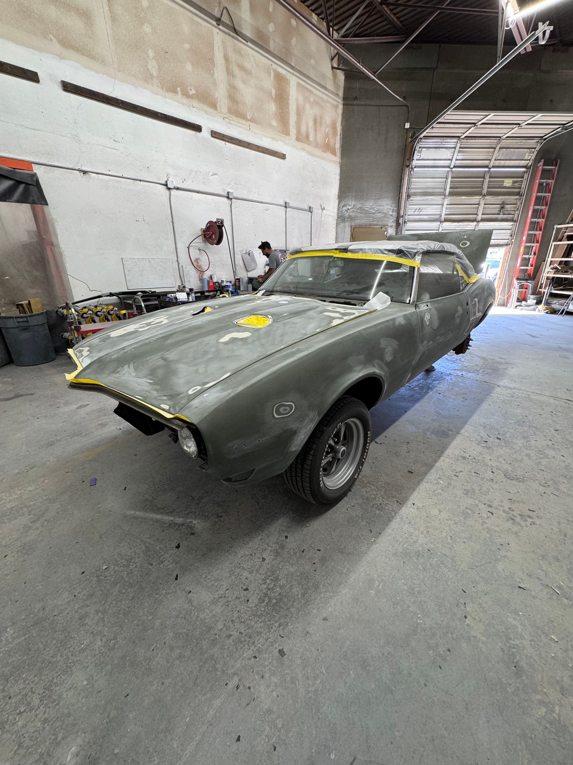 Partially restored classic car shell in a workshop garage, gray body with missing front parts