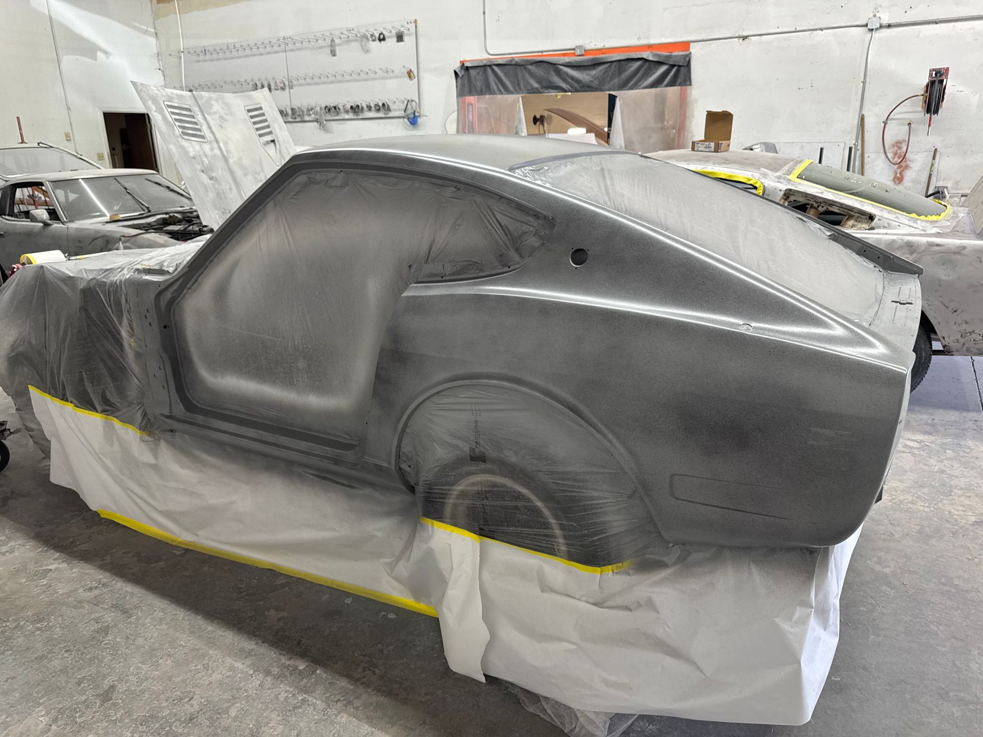 Black car body shell in a workshop, masked with tape and paper for painting, side view