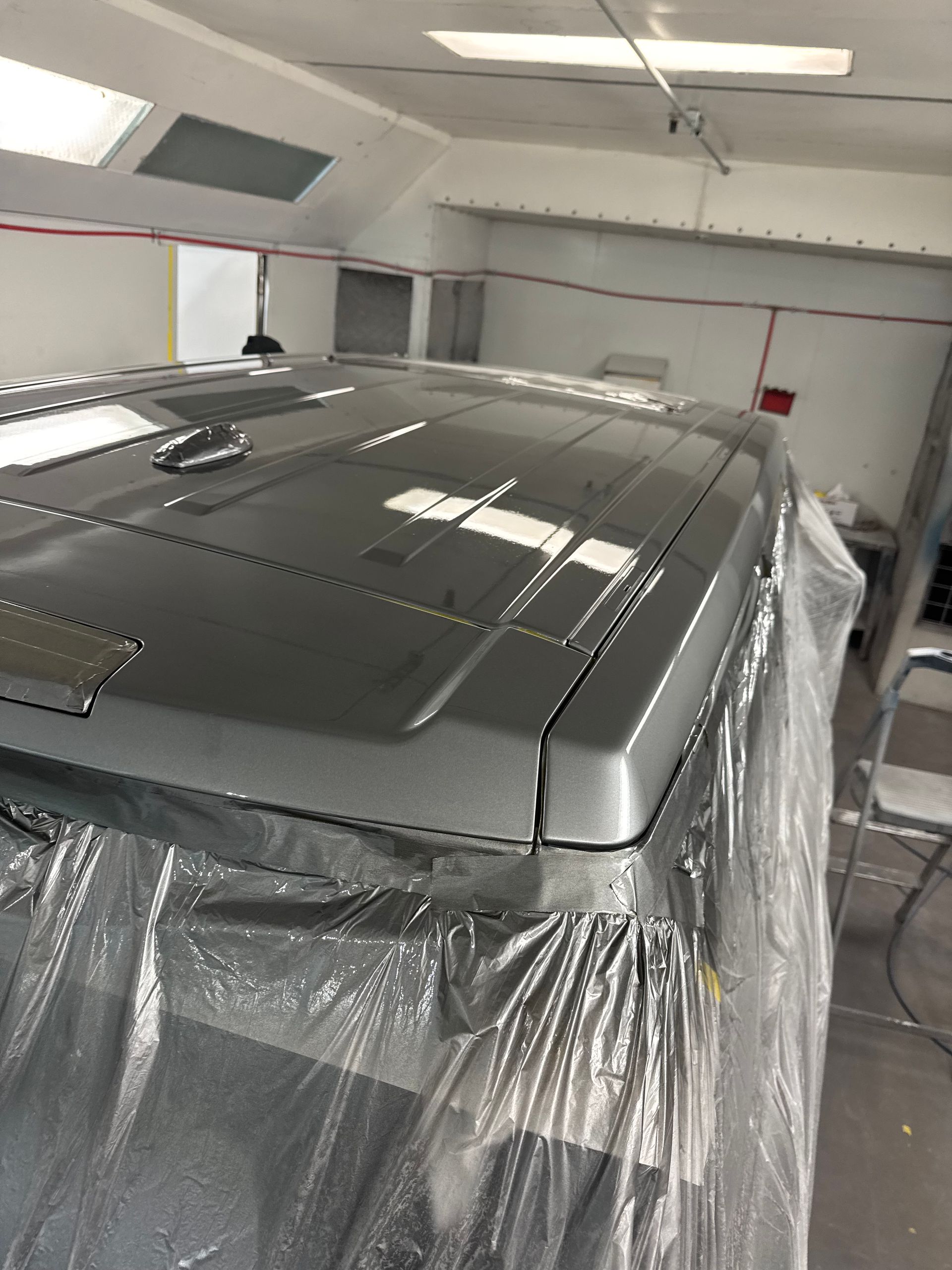 Gray vehicle in a spray booth, partially covered with plastic masking sheets.