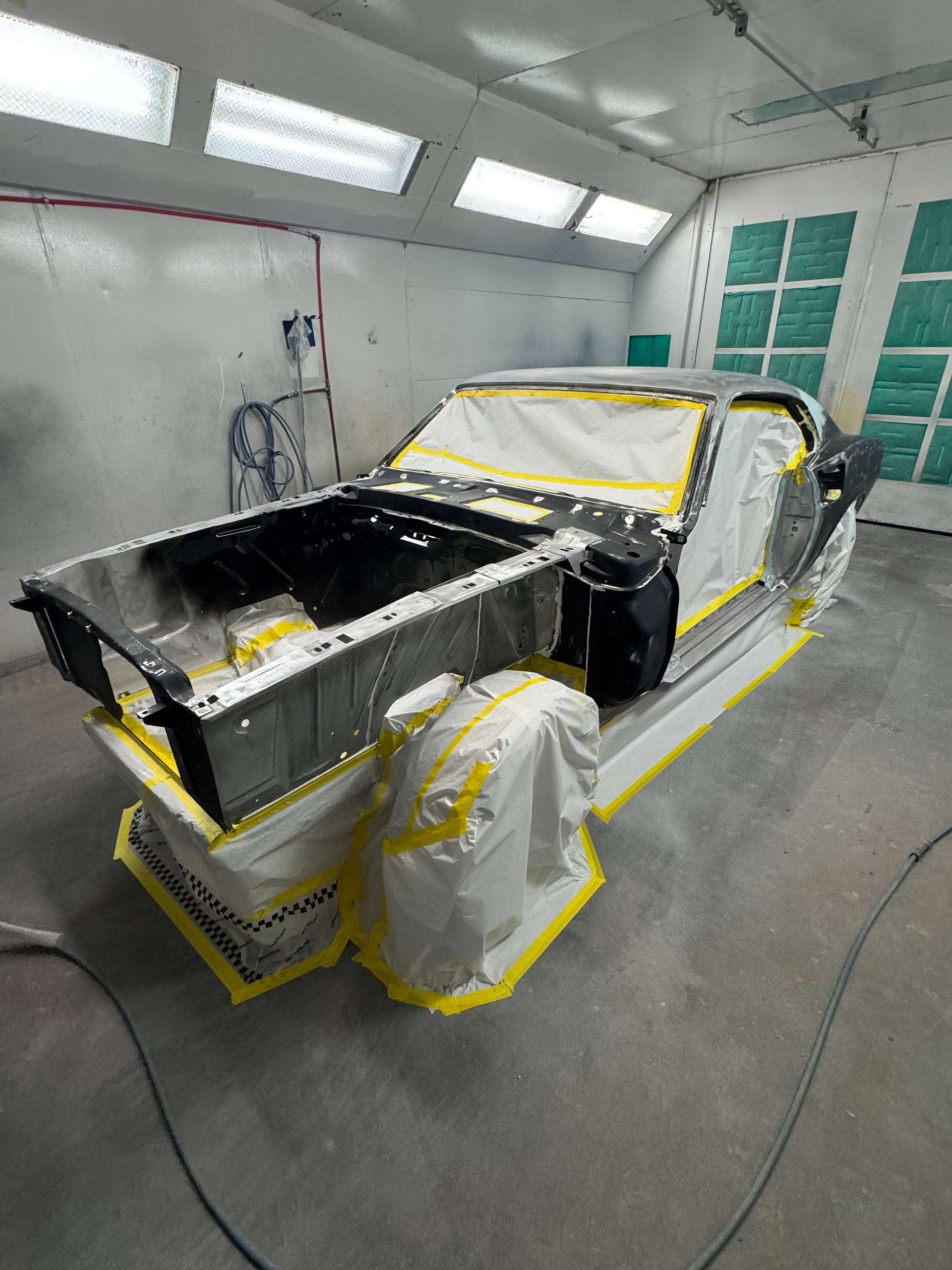 Car body in a paint booth, masked with tape and plastic sheeting, ready for refinishing