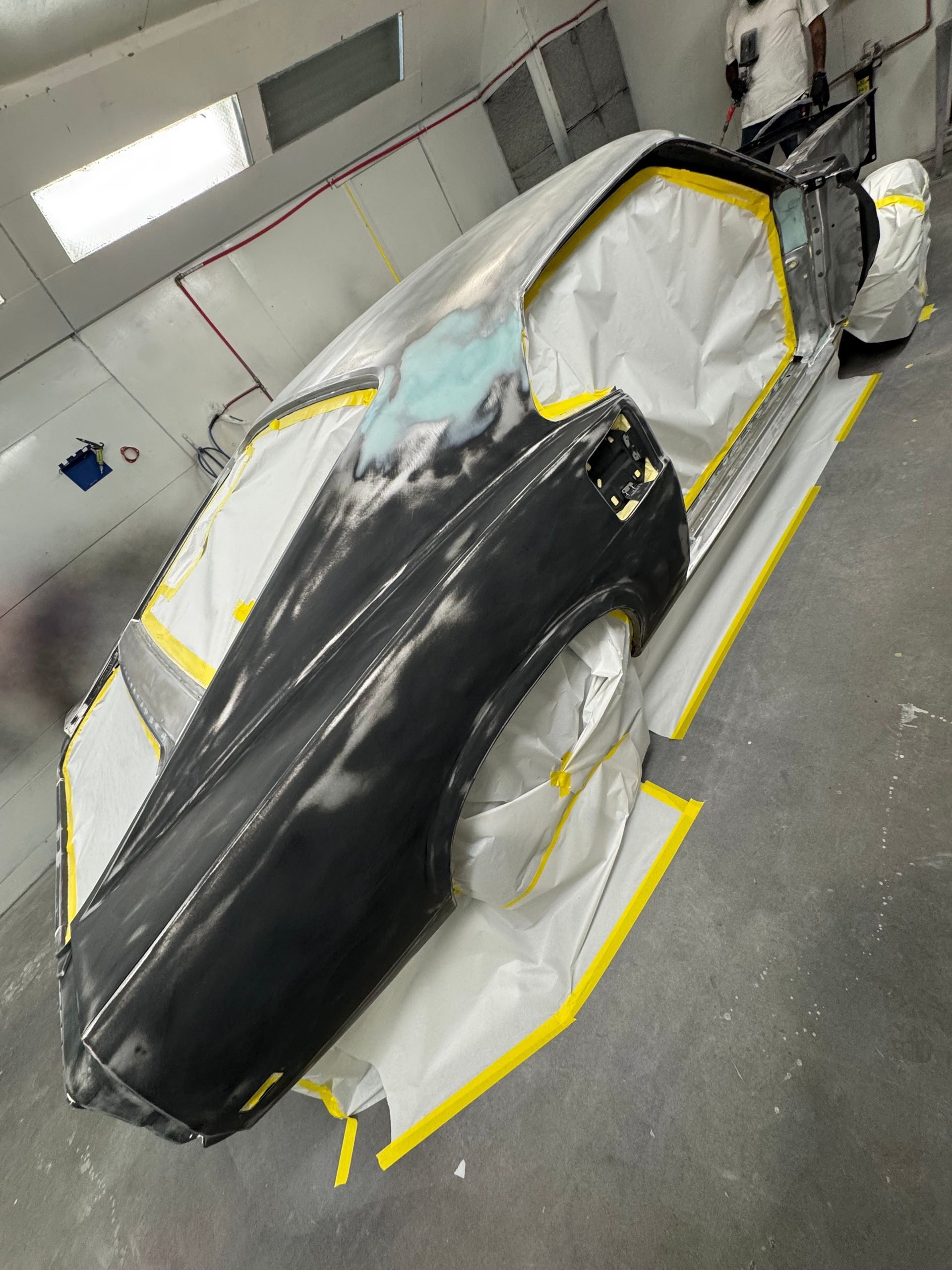 Car under repair, masked with plastic and tape in a body shop, black hood exposed
