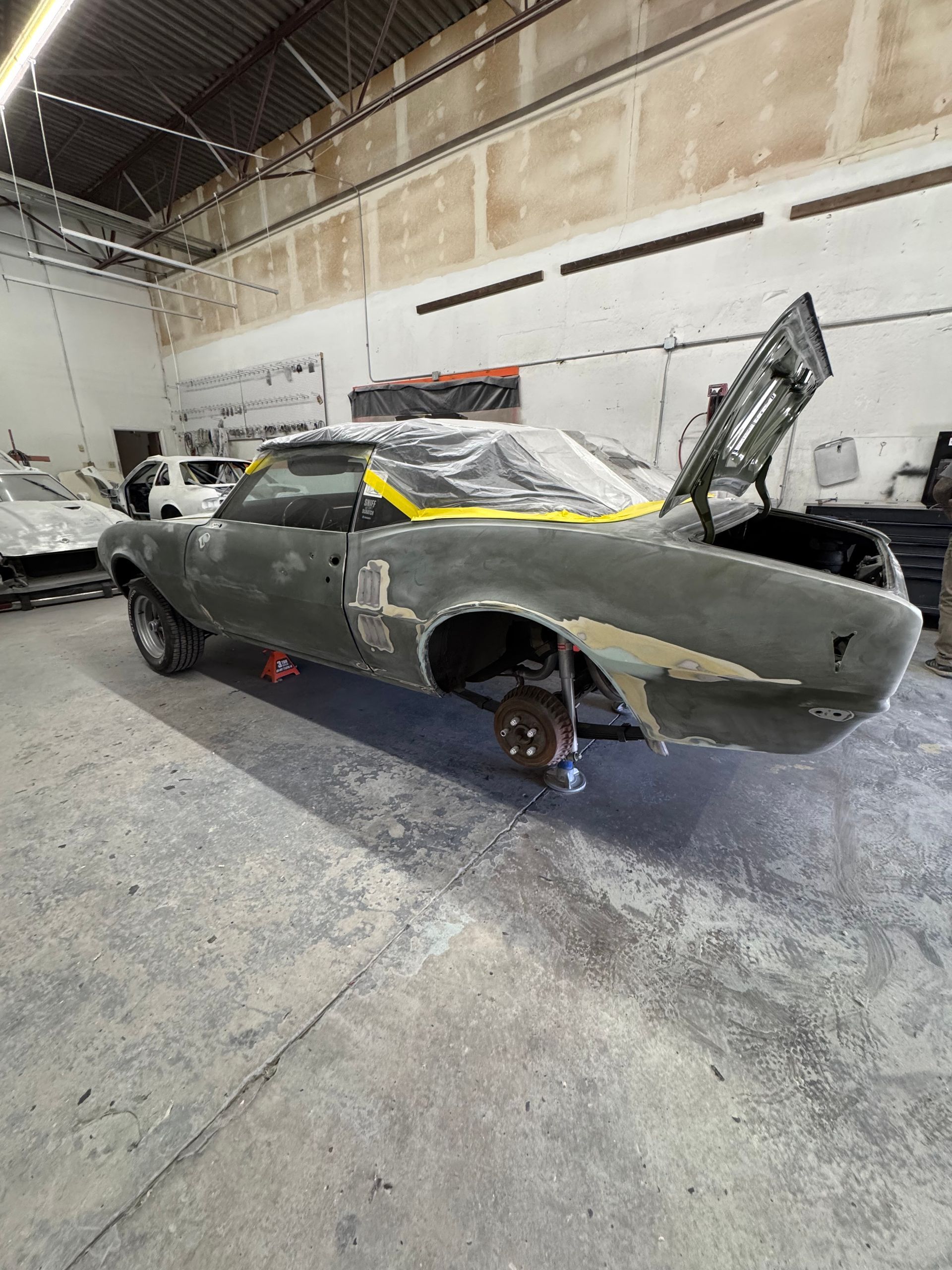 Partially restored gray sports car in a workshop, with its hood open and front wheel removed.