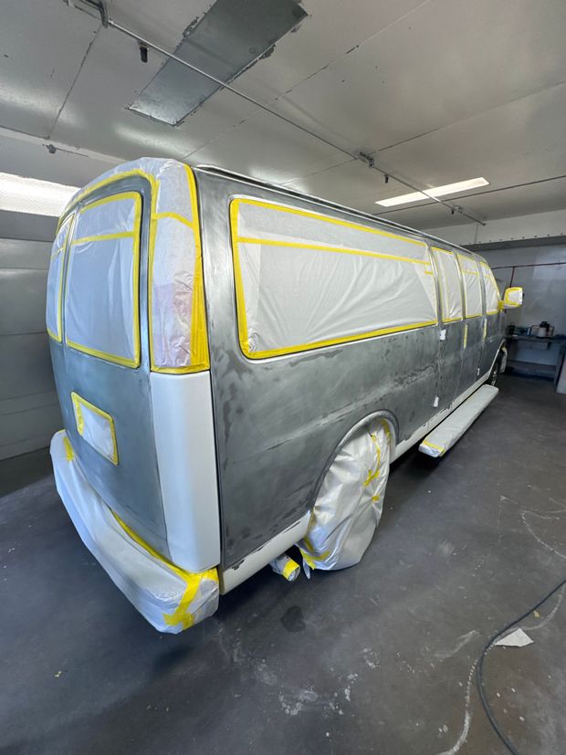 Masked vehicle in a garage, covered with gray plastic and yellow painter’s tape for painting.