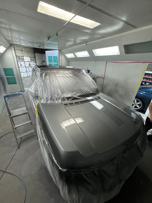 Car covered in plastic inside a paint booth, with a ladder beside it.