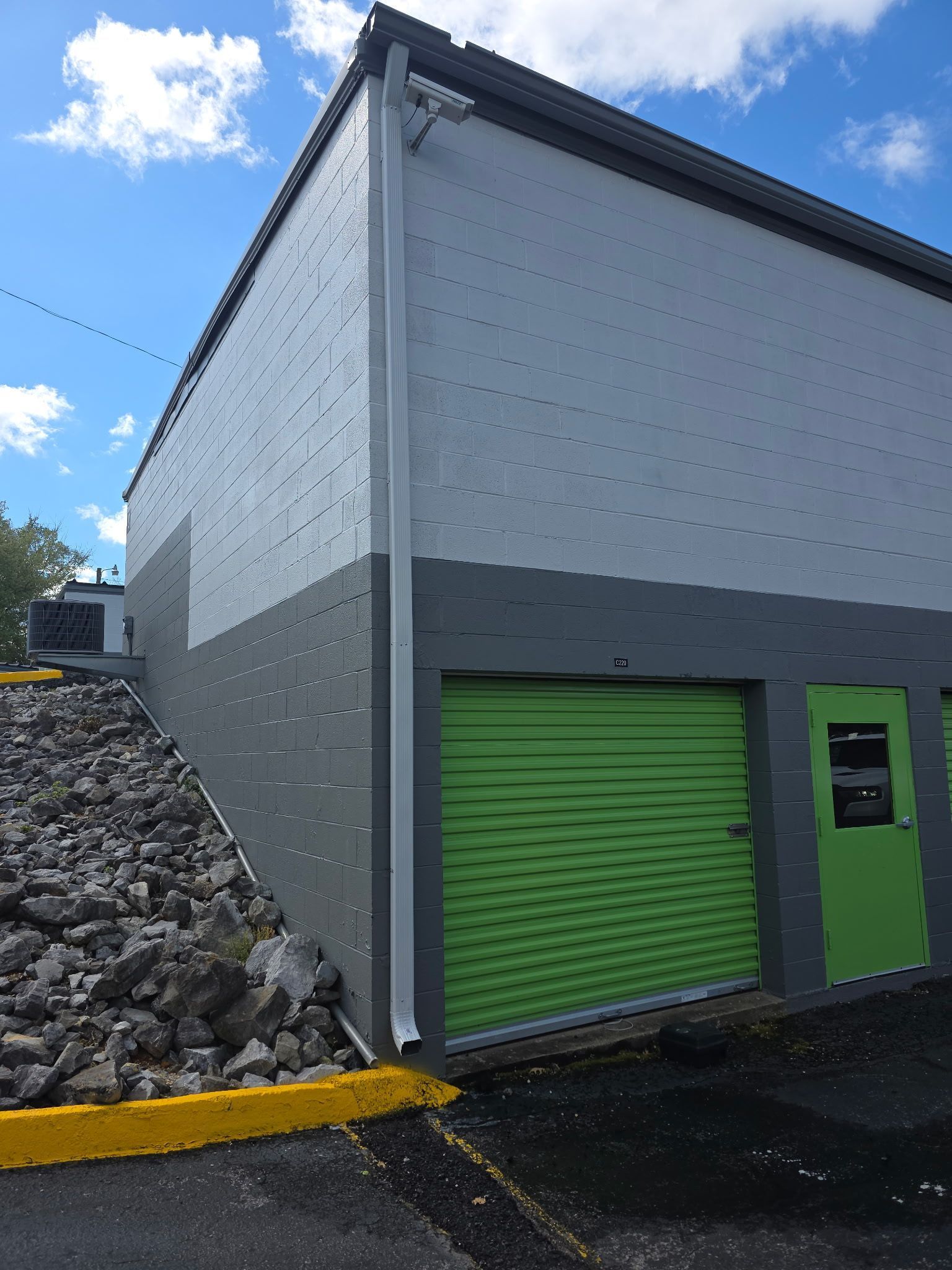 A grey concrete storage building featuring a bright green roll-up door and a side entry door next to a rock embankment.