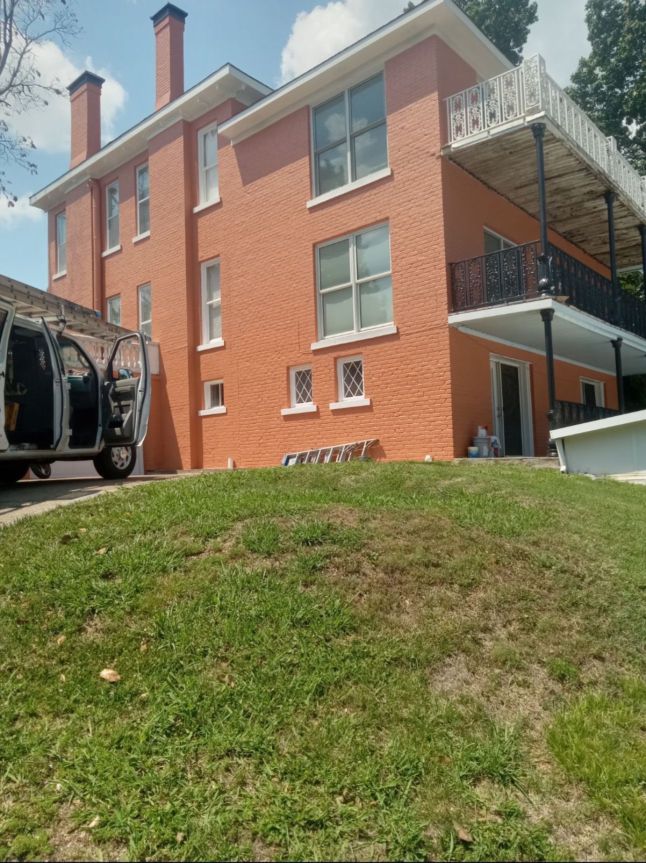 Brick building painted orange with white trim, two-story with a balcony, set on a grassy hill.