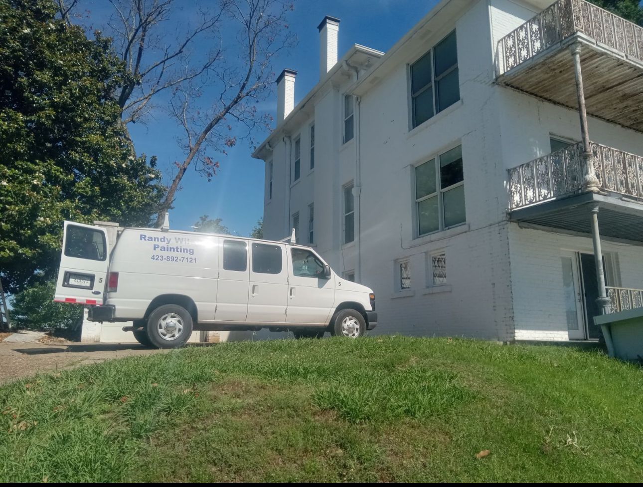 White van parked next to a white multi-story building on a grassy hill under a blue sky.