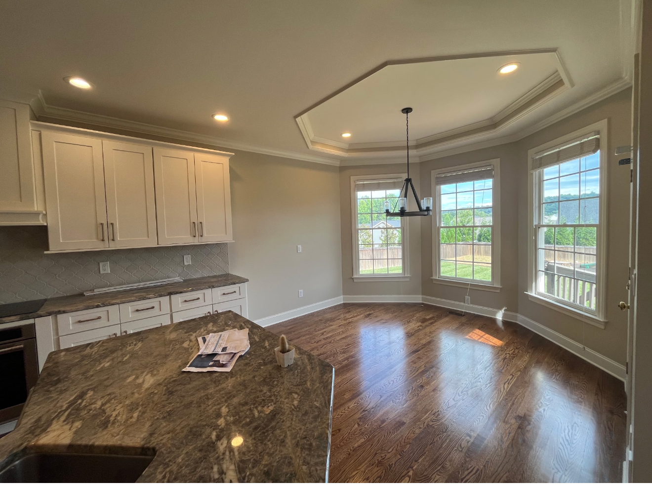 Spacious kitchen with white cabinets, granite island, and large bay windows overlooking a yard.