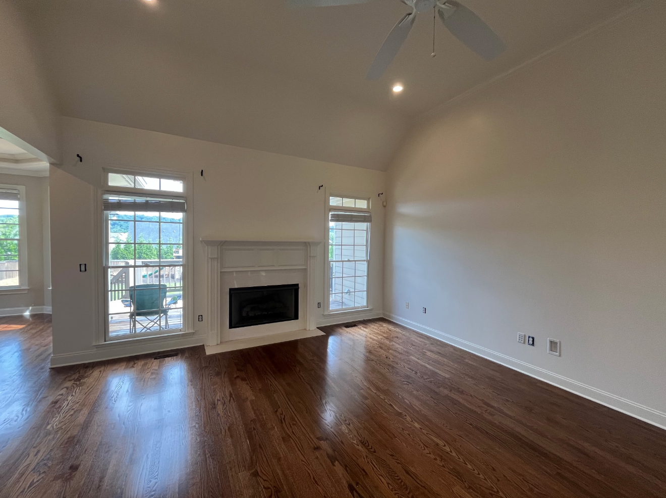 Empty living room with hardwood floors, white walls, fireplace, and tall windows with natural light