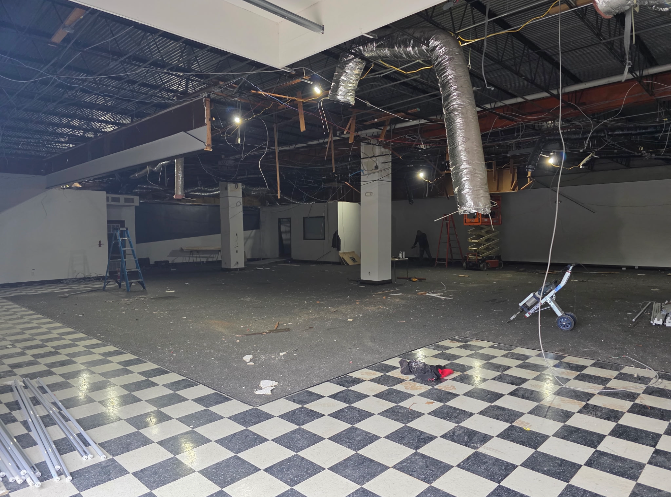 Damaged indoor space with debris, hanging ductwork, and checkered floor tiles; looks like a vacant commercial area