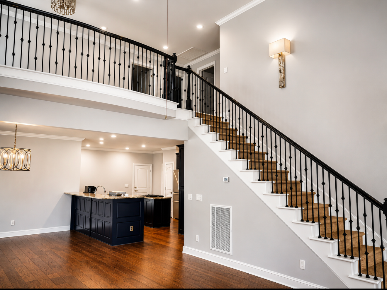 Bright modern foyer with a black staircase, white walls, wood floors, and a kitchen below the landing