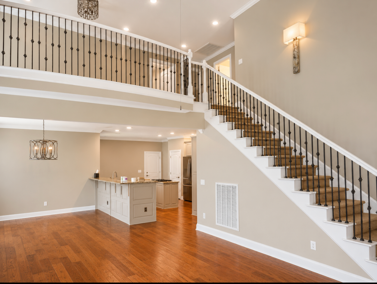Bright living room with hardwood floors, staircase, and open kitchen under a loft balcony
