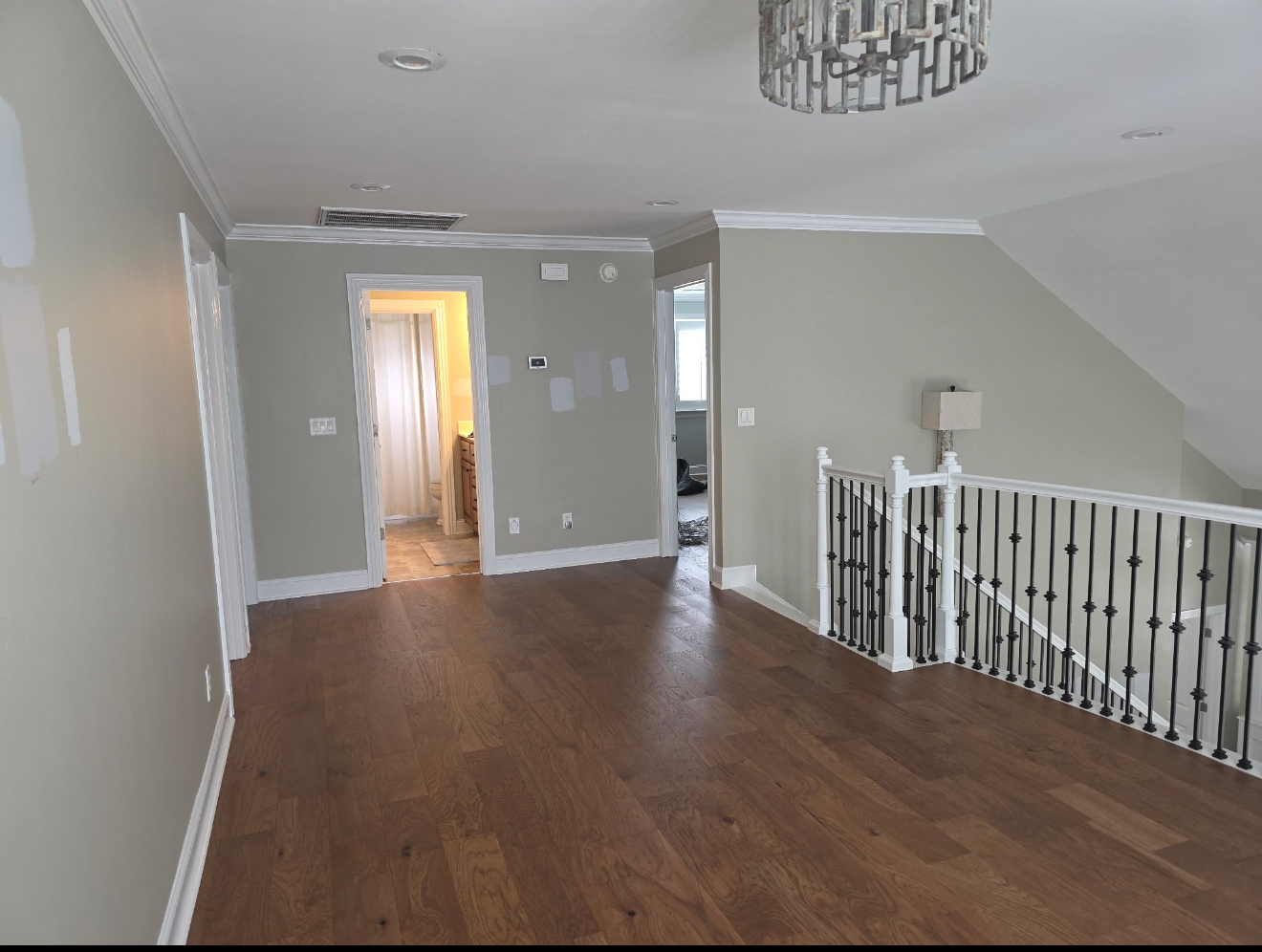 Bright hallway with hardwood floors, gray walls, chandelier, and white stair railing leading to upper floor.