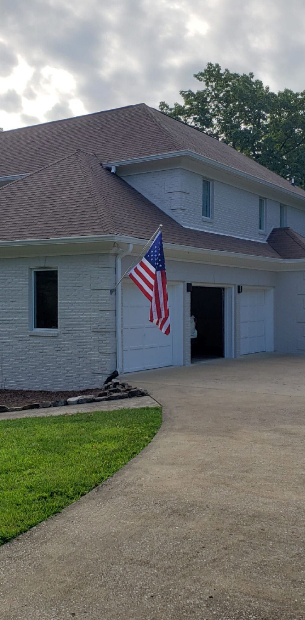A house with an American flag hanging by the garage, cloudy sky.