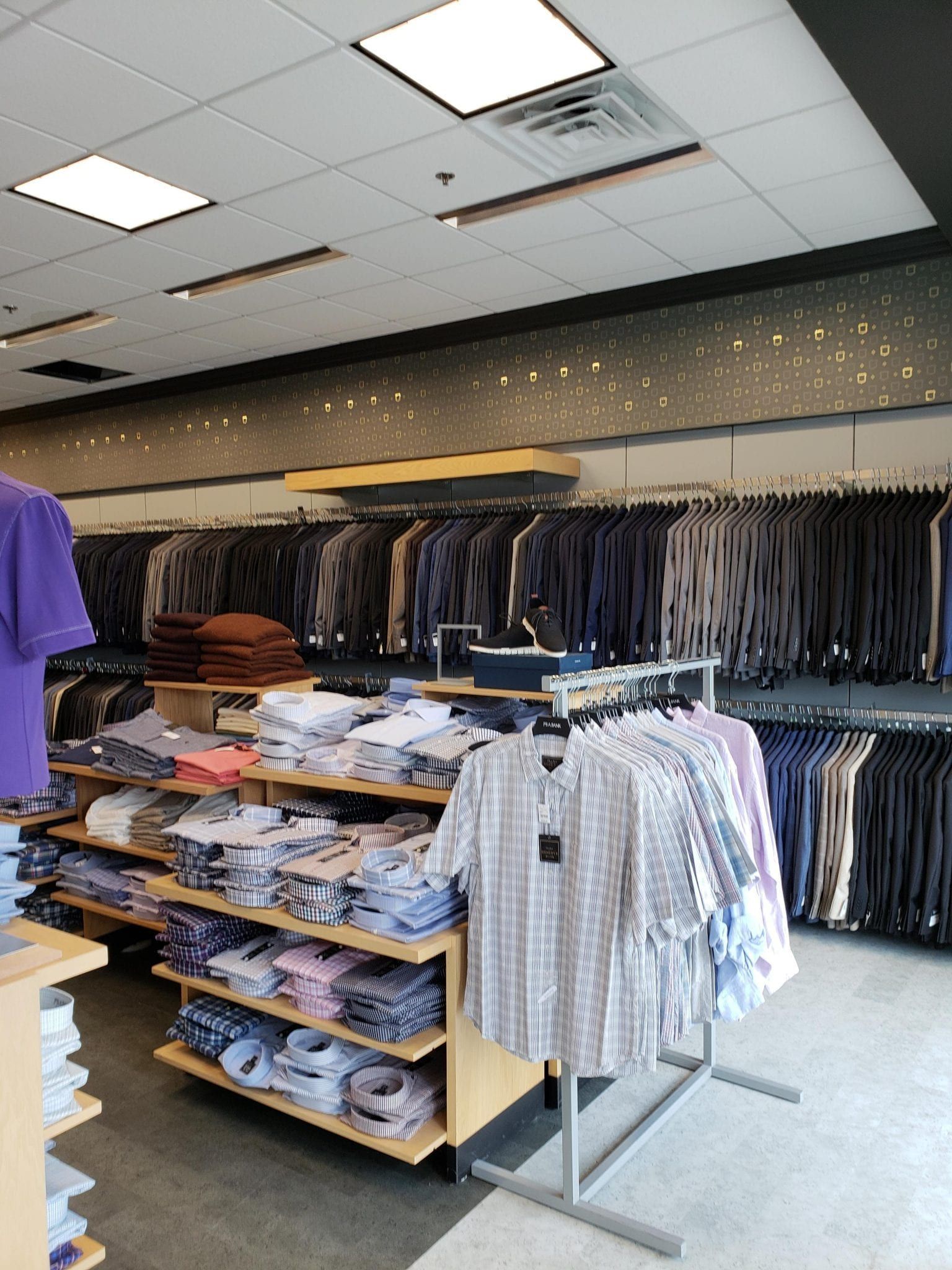Clothing store interior; shirts and suits on display; neutral tones, bright overhead lights.