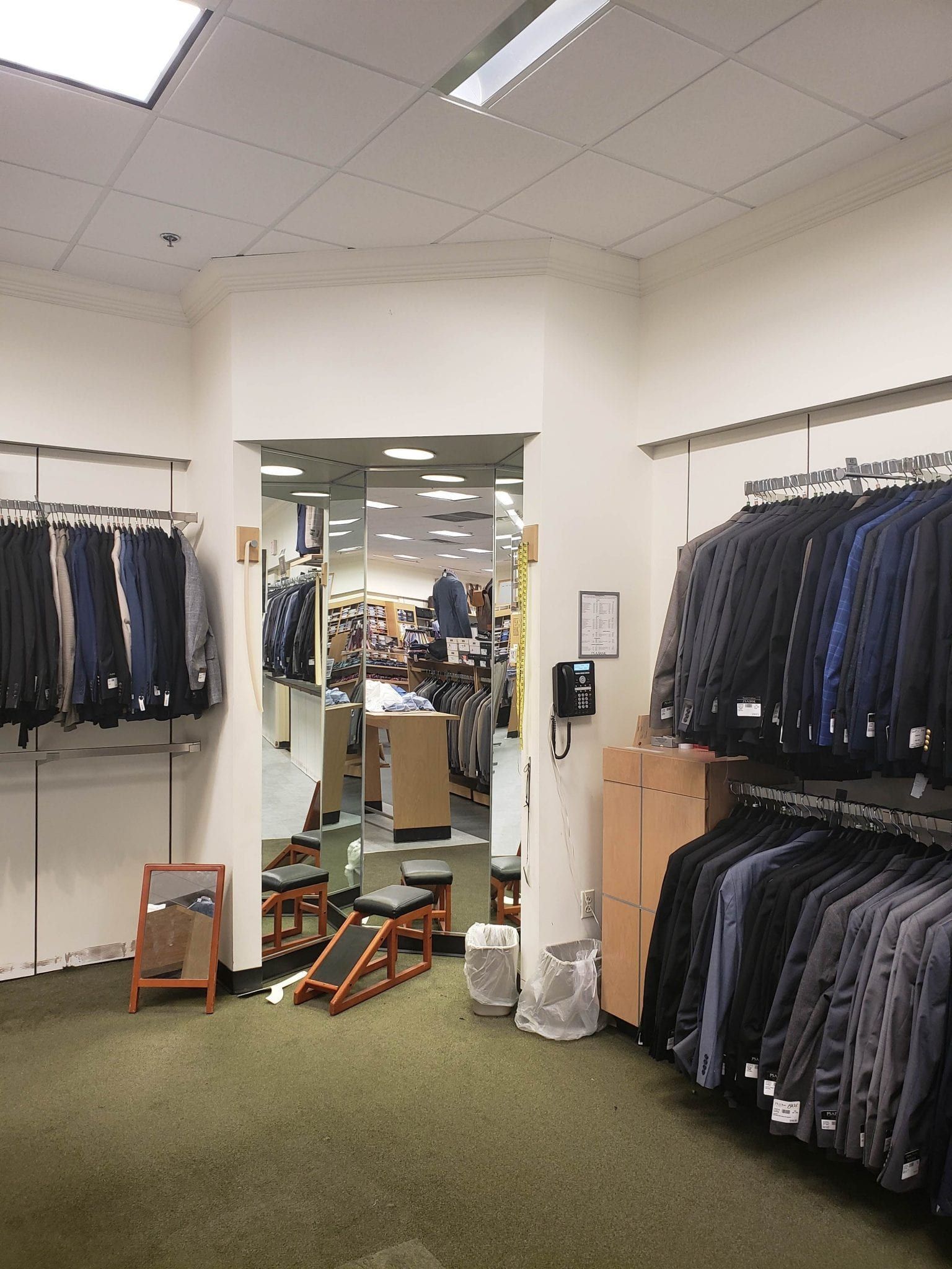 Clothing store interior; racks of suits, doorway to other aisles, green carpet, various accessories.