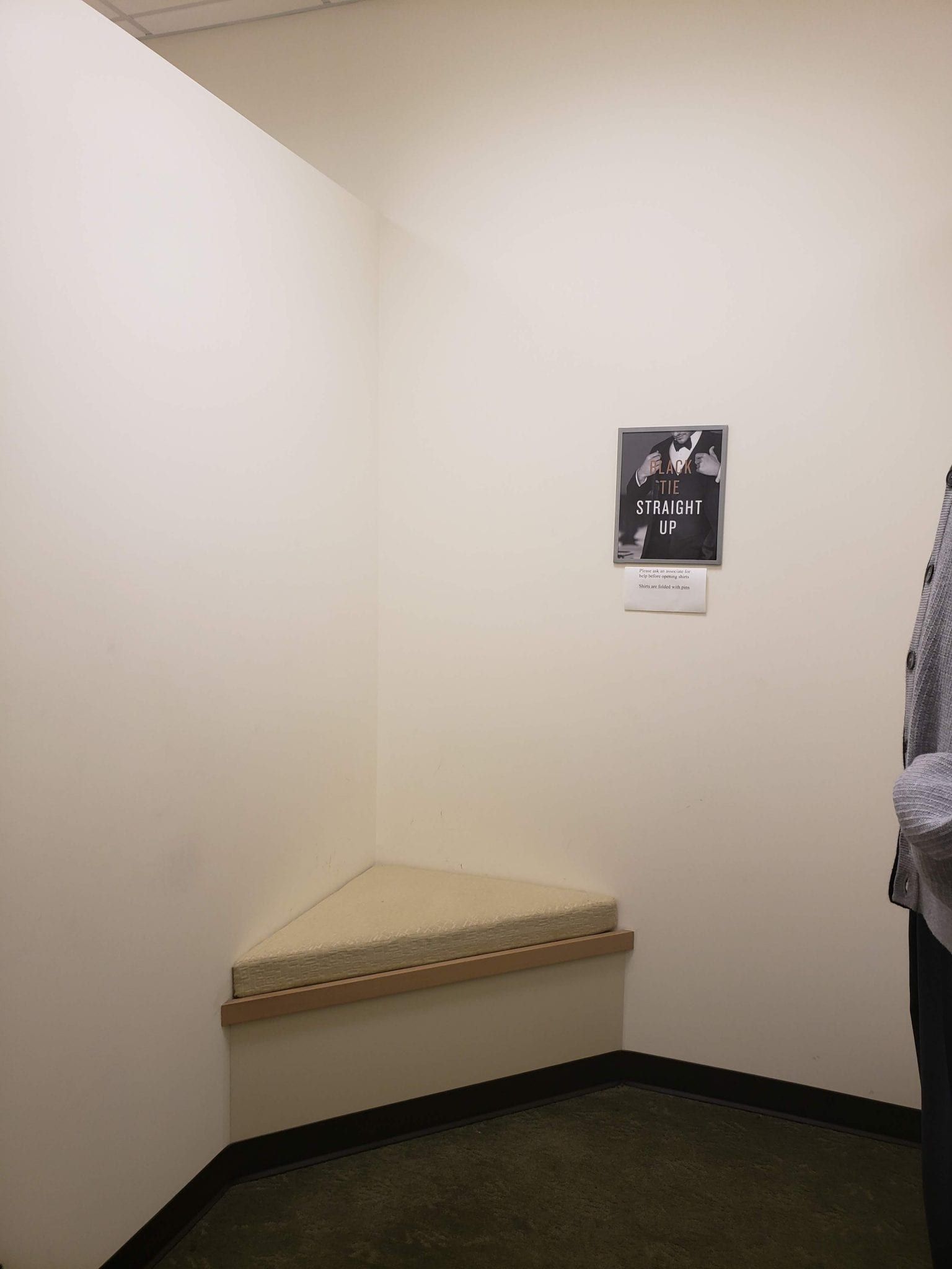 Corner of a room with a triangular bench. Black and white photo hangs on the wall.