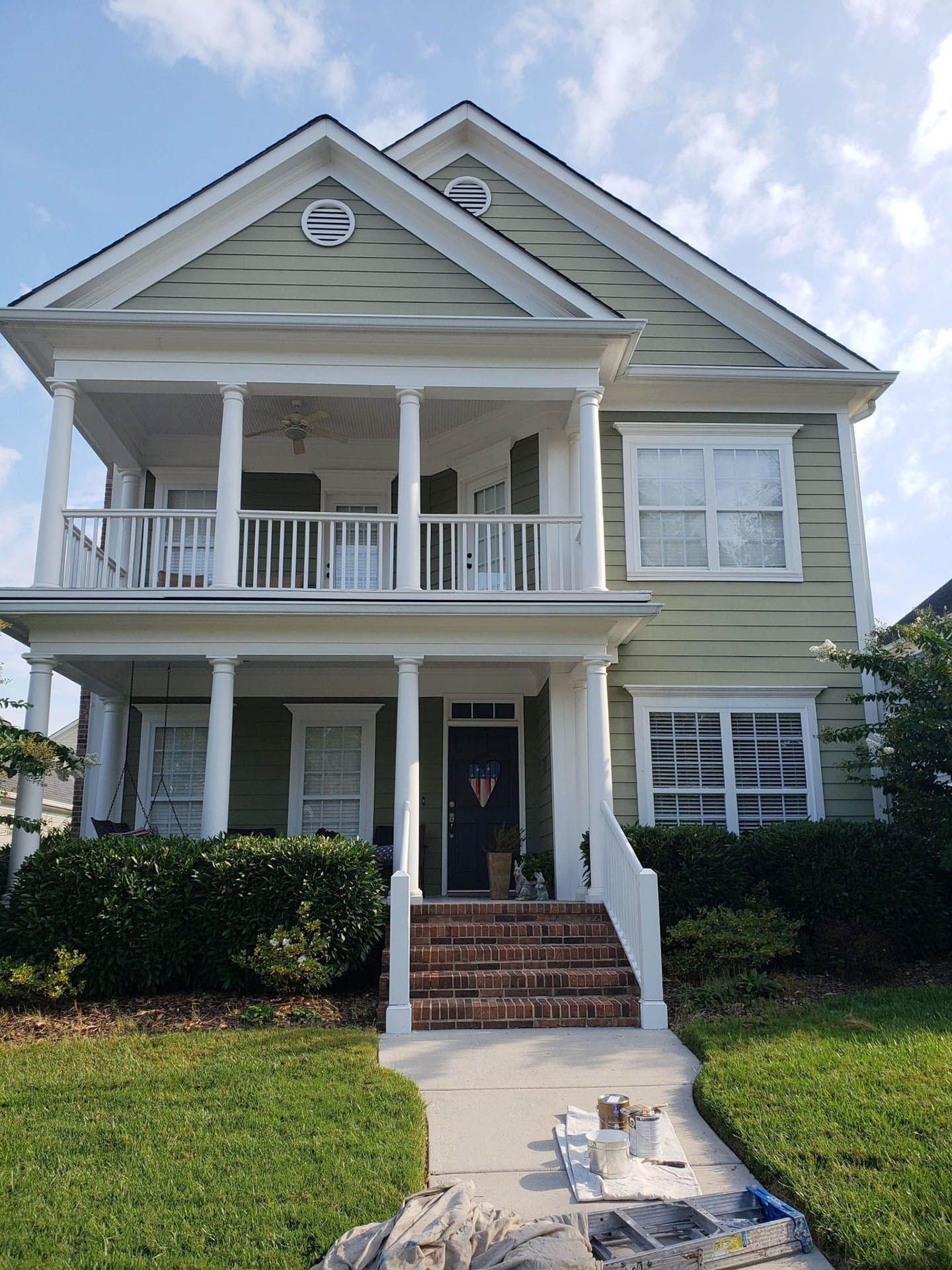 Two-story green house with white trim, porch, blue door, and brick stairs.
