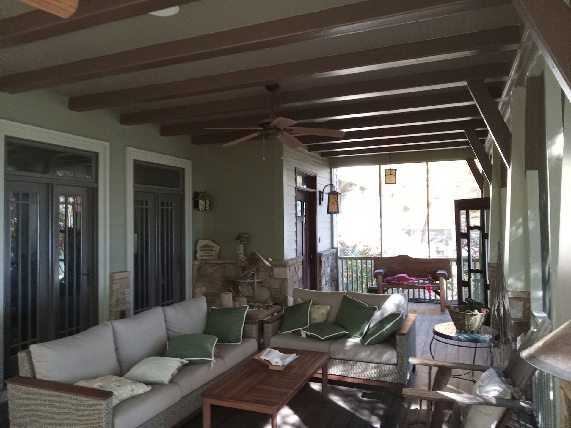 Covered porch with seating couches, chairs, wooden ceiling beams, olive green walls, and screened openings.