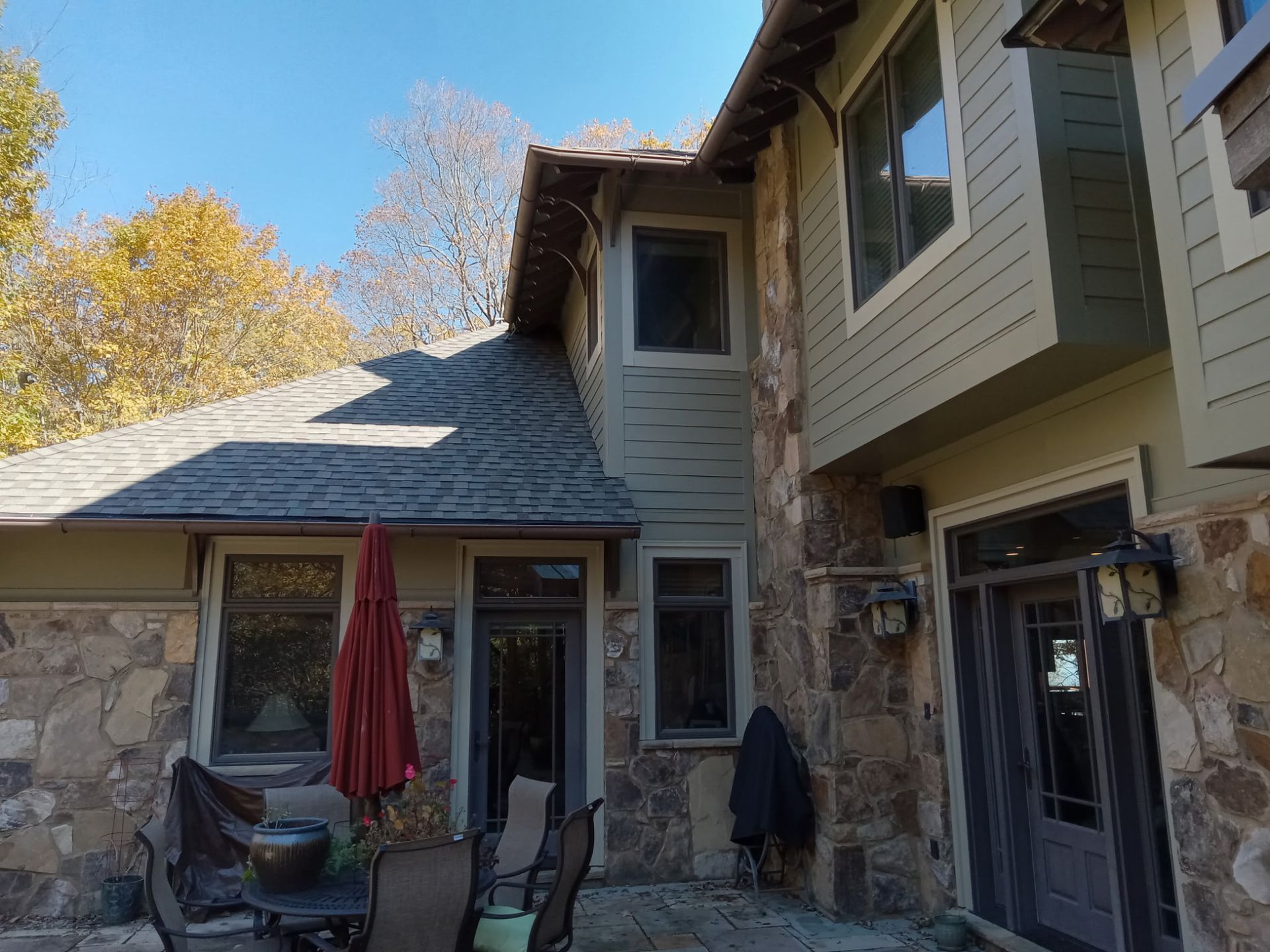 Exterior view of a house with stone and green siding, windows, and an open patio with furniture.