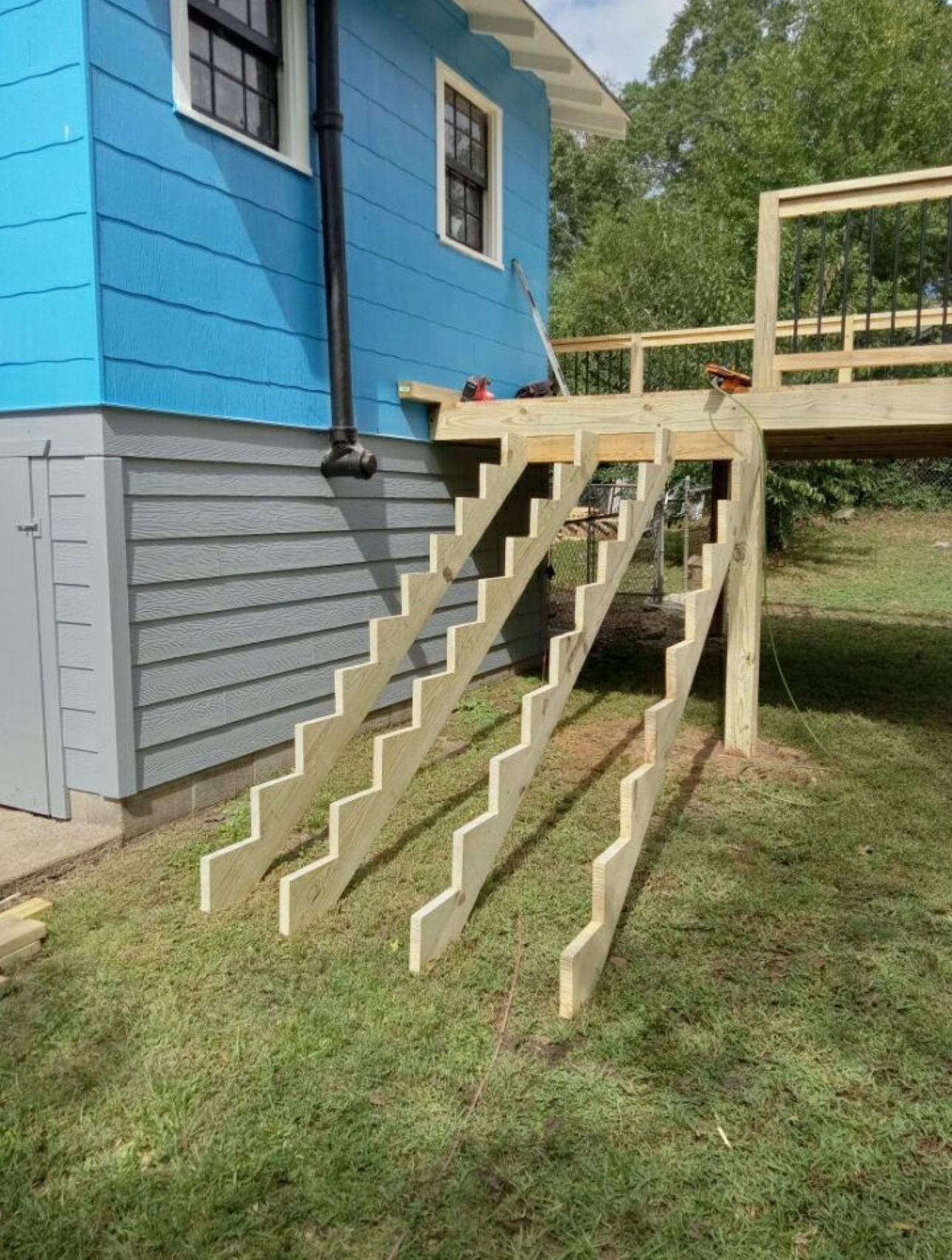 Wooden staircase being built next to a blue house and a deck in a grassy backyard