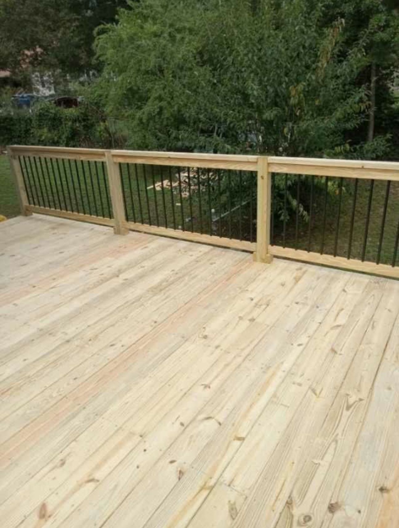 Wooden deck with black railing, surrounded by green trees and grass