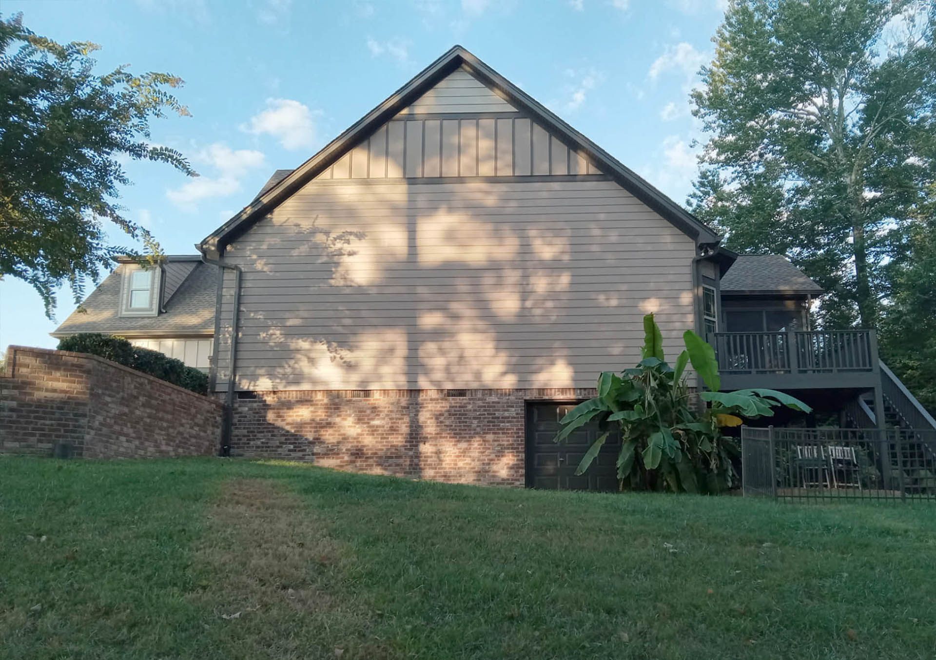 Back of a house on a grassy hill, with a brick foundation, wooden siding, and a deck