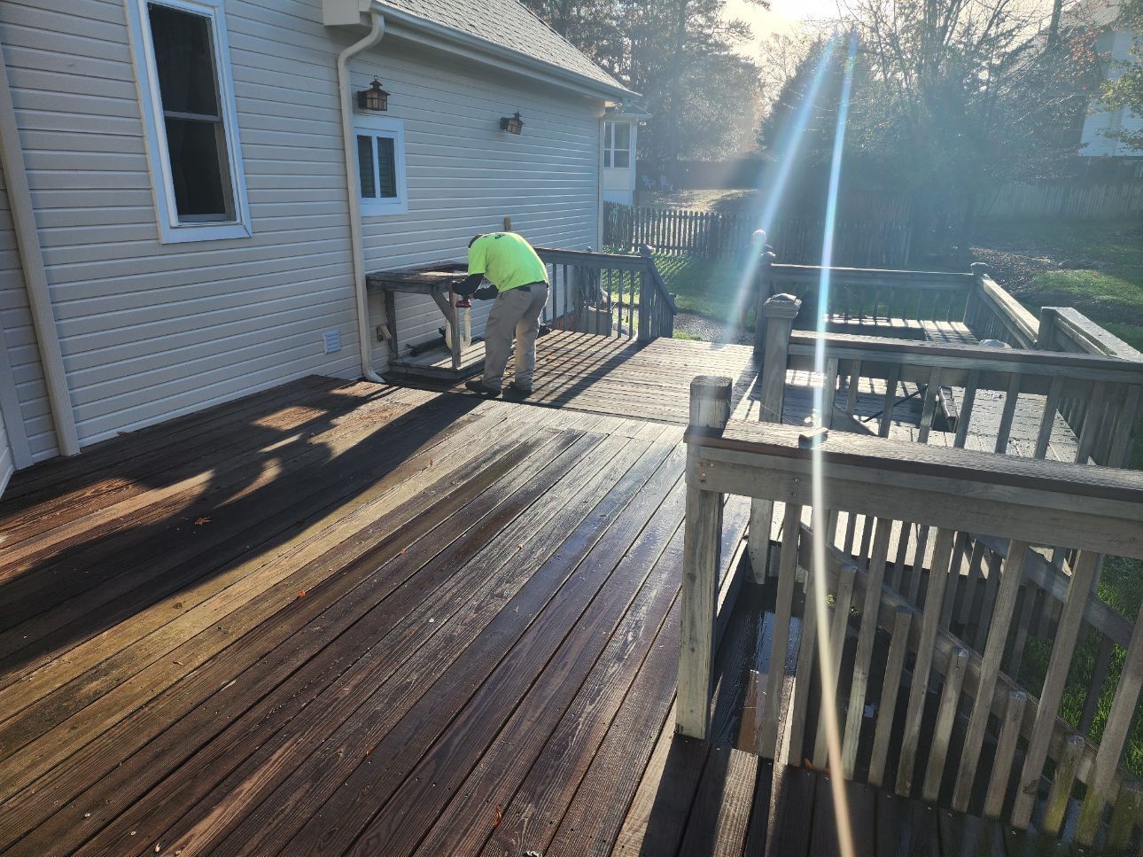 A man is cleaning a wooden deck in front of a house