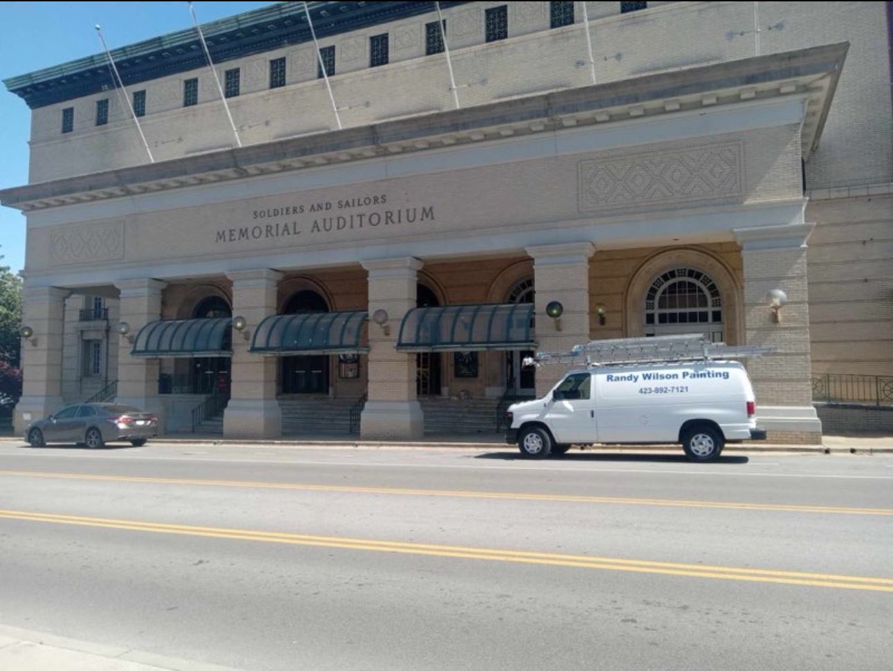 A white van is parked in front of a large building
