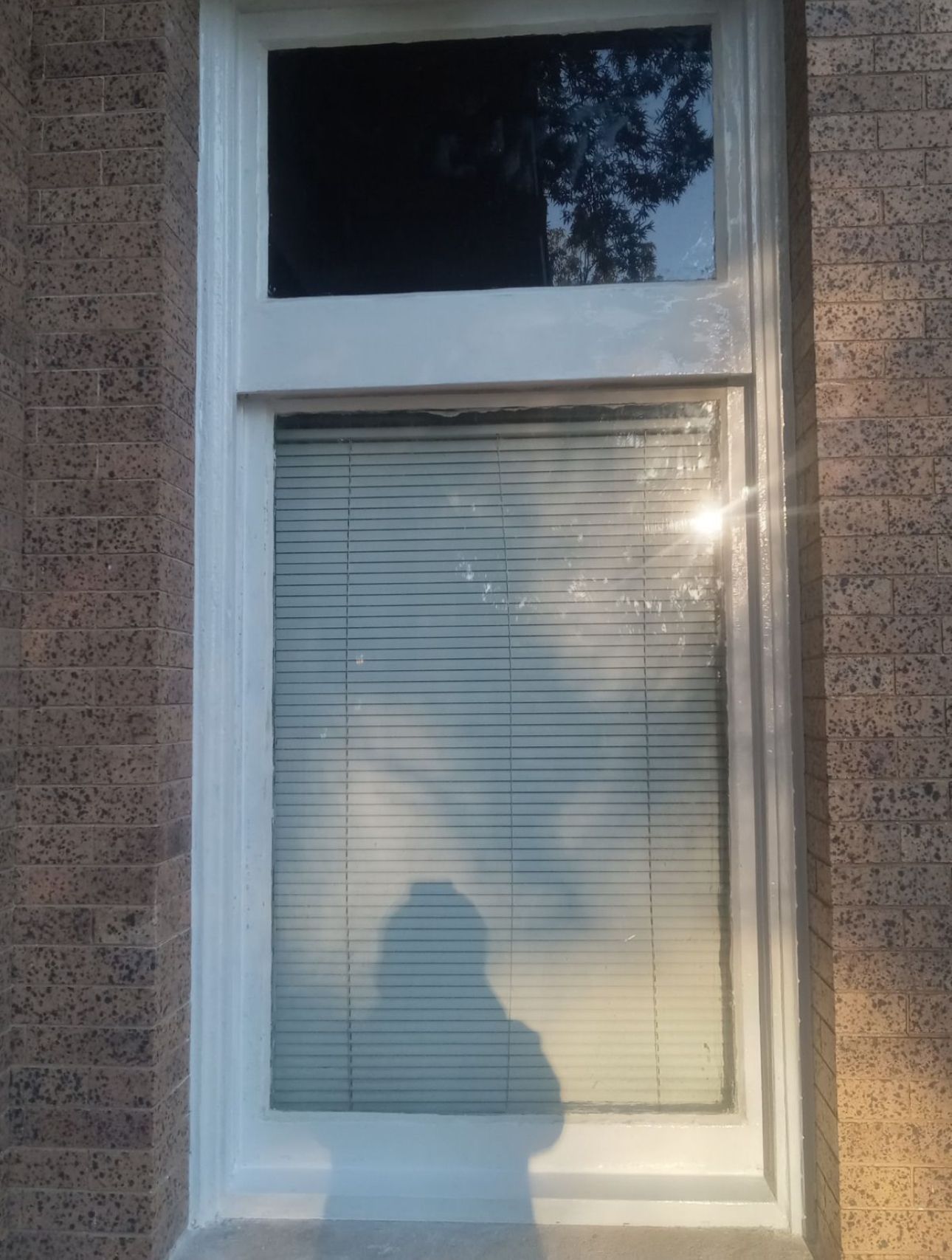 A white window with blinds on a brick building